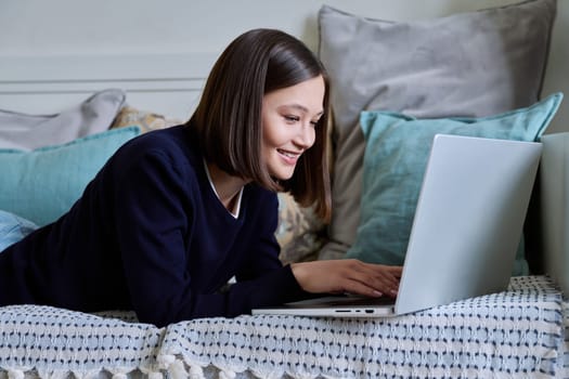 Young woman using laptop computer, typing on keyboard, lying on sofa at home. Internet online technologies for work communication study leisure