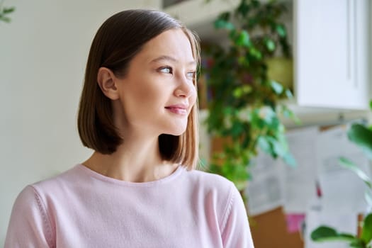 Portrait of young attractive smiling woman in home interior. Happy cheerful relaxed 20s female looking away, at window, copy space. Beauty, youth, happiness, health, lifestyle concept