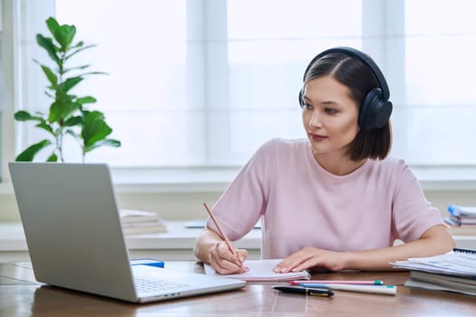 Young female in headphones using computer laptop for studying, university college student studying at home, writing typing. Technology, education, training, youth concept