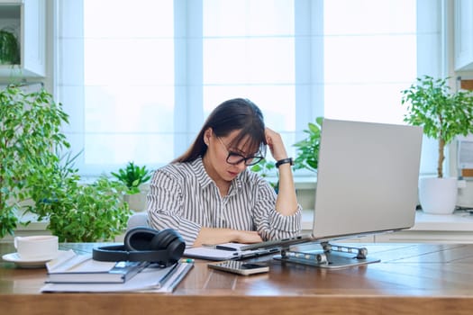 Sad upset tired businesswoman sitting at workplace with computer laptop in home office. Difficulties, problems in business, work