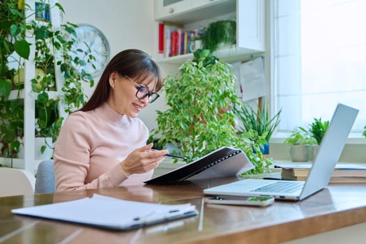 Woman working remotely in home office at workplace with computer. Female professional holding paper contract in hands, architect lawyer accountant preparing documents. Work remotely business freelance