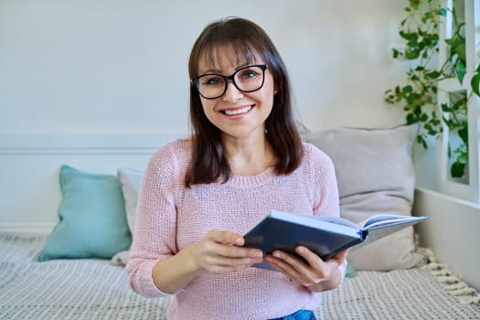 Webcam view of middle-aged woman talking during video call chat conference, female looking at camera holding notebook working remotely at home. Webinar, online meeting consultation teaching interview