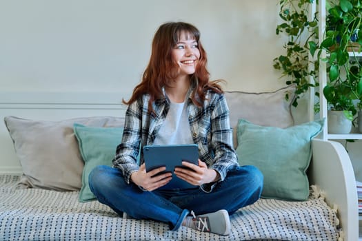 Young attractive trendy girl college student using digital tablet for studying communication leisure freelancing, sitting on couch at home. Technology, youth, education, lifestyle concept