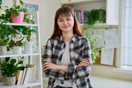 Portrait of female teenager 18-20 years old, smiling confident looking at camera with crossed arms in home. Beautiful girl with nose piercing, trendy makeup hairstyle. Youth lifestyle beauty fashion