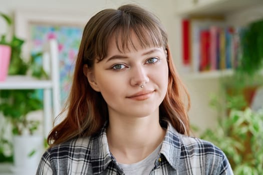 Portrait of female teenager 18-20 years old, smiling looking at camera in home. Beautiful girl with nose piercing, trendy makeup hairstyle. Youth lifestyle beauty fashion