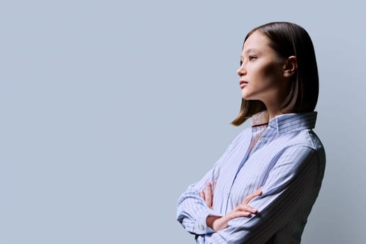 Profile view, confident serious successful young business woman with crossed arms, copy space gray studio background, space for advertising image text. Business work services education people concept