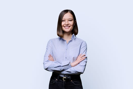 Young confident smiling business woman with crossed arms on white studio background. Positive happy female in shirt, student worker owner entrepreneur looking at camera. Business work education people