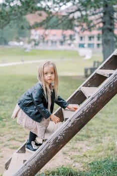 Little girl climbing a wooden ladder on a playground in a park, looking away. High quality photo