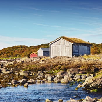 Norway, house and outdoor in field, lake and rocks for travel and holiday in background with hills. Shed, grass and blue sky for cottage, serenity and sunlight for nature in season for countryside.