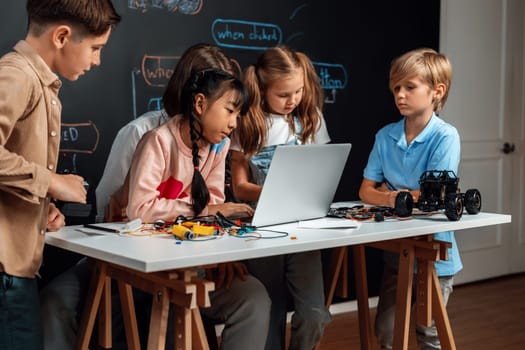 Skilled kids learning to program remote car. Schoolgirl in pink cloth use laptop for coding. Other child watch her code while teacher watch her. motherboard and electric wire also on table. Erudition.