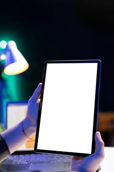 Closeup of a tablet held by an individual is showing an isolated white screen. Selective focus of digital device displaying blank chromakey mockup template.