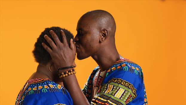African american man kissing his wife forehead on camera and expressing sincere true feelings for her, sweet affection. Husband doing romantic gesture in studio, caring about his partner.