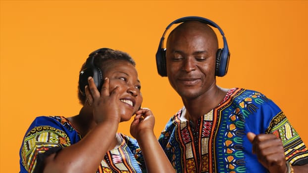 African american partners dancing on headset music in studio, having fun together with cool groovy songs. Ethnic couple doing funky dance moves and feeling relaxed with headphones.