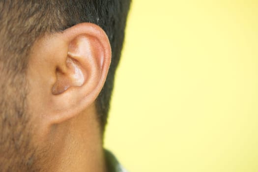 Close up of young man ear with a yellow background