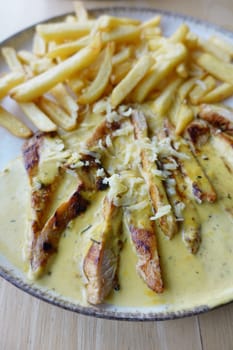 Ready to eat sliced chicken with cream sauce with french fries on a plate .