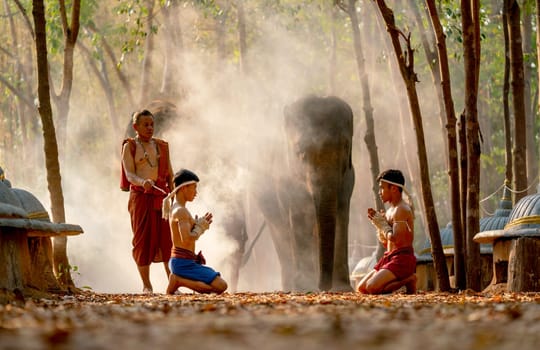 Two Asian men sit and action with traditional martial art fight position before start of fighting and teacher stand beside with elephant on background.