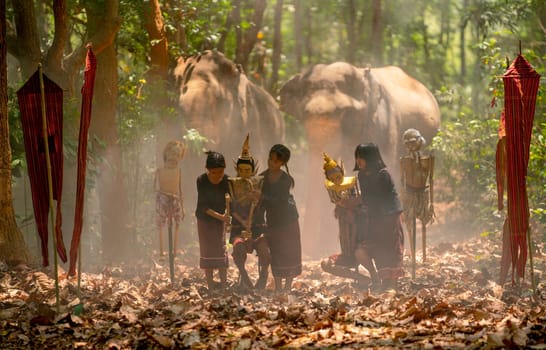 Group of Asian children show or practice manipulate the puppets in  front of big elephant in walkway in jungle and they look happy for this  traditional culture.