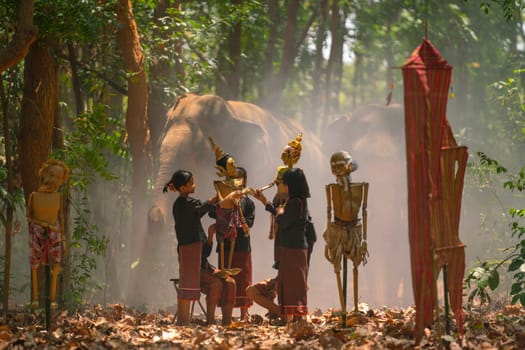 Group of Asian children show or practice manipulate the puppets in  front of big elephant in walkway in jungle and they look happy for this  traditional culture.