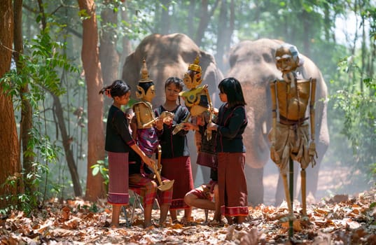 Group of Asian boys and girl enjoy to show or practice manipulate the puppets in  front of big elephant in walkway in jungle and they look happy for this  traditional culture.