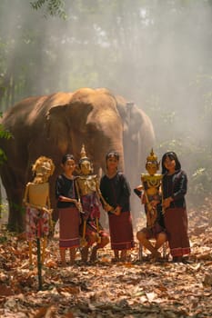 Vertical image of group of Asian children show or practice manipulate the puppets in  front of big elephant in walkway in jungle and they look happy for this  traditional culture.
