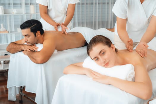 Caucasian couple customer enjoying relaxing anti-stress spa massage and pampering with beauty skin recreation leisure in day light ambient salon spa at luxury resort or hotel. Quiescent