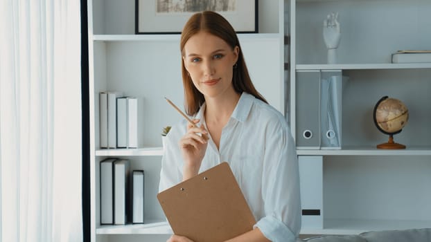 Friendly psychologist woman in clinic office professional portrait with smile and holding clipboard for patient to visit psychologist. The experienced and prim confident psychologist