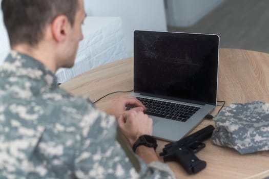 Young hispanic man army soldier using laptop sitting on table at home. High quality photo