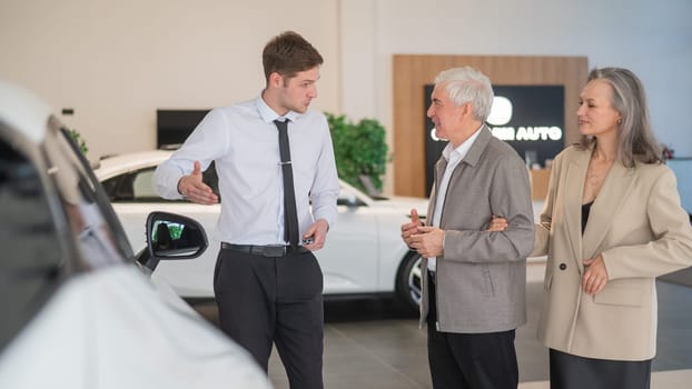 A salesman in a car dealership shows a car to a mature married couple