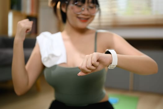 Smiling young woman checking results on smartwatch after home workout.
