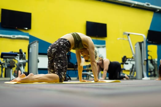 slender athletic woman in the gym is beautifully engaged in yoga exercises on a mat