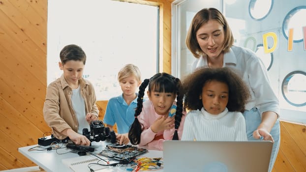 Caucasian teacher praise student while looking at learner work or presentation. Group of diverse student looking at presentation and fixing motherboard at table with chips and wires placed. Erudition.