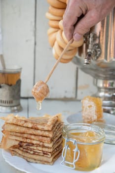 A man pours honey on pancakes and drinks tea from a samovar, Russian tradition of celebrating Maslenitsa. High quality photo