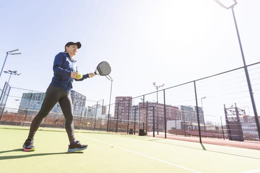 A girl in sportswear is training on a paddle tennis court. The girl is hitting the ball against the glass to make a rebound. Concept of women playing paddle. High quality photo