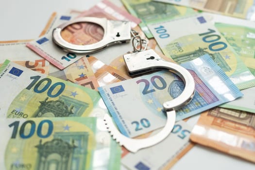 Pair of metal police handcuffs on Euros banknotes money cash background. Corruption, dirty money, gambling or financial crime ideas concept. High quality photo