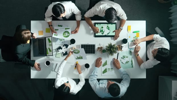 Top down view of business team discussing about using clean energy and sustainable investment at meeting table with wind mill, document with environmental graph and wooden house model. Alimentation.