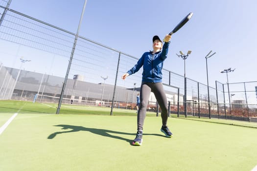 A girl in sportswear is training on a paddle tennis court. The girl is hitting the ball against the glass to make a rebound. Concept of women playing paddle. High quality photo