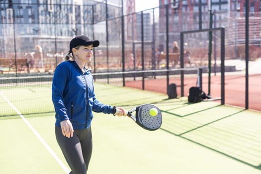 A girl in sportswear is training on a paddle tennis court. The girl is hitting the ball against the glass to make a rebound. Concept of women playing paddle. High quality photo