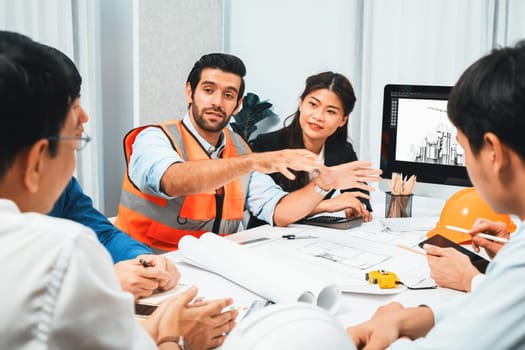 Diverse group of civil engineer and client working together on architectural project, reviewing construction plan and building blueprint at meeting table. Prudent