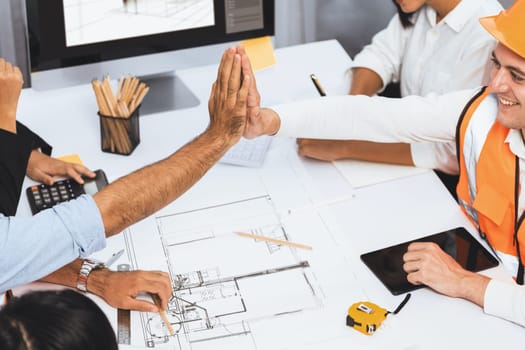 Diverse group of civil engineer and client celebrate and high five after make successful agreement on architectural project, reviewing construction plan and building blueprint at meeting table.Prudent