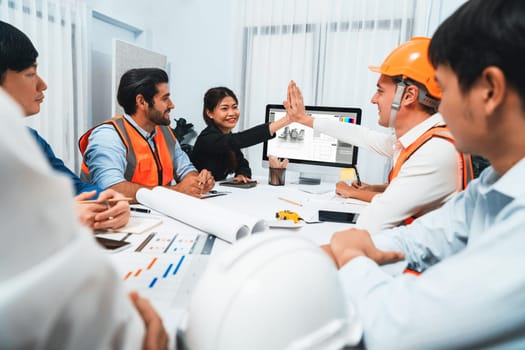 Diverse group of civil engineer and client celebrate and high five after make successful agreement on architectural project, reviewing construction plan and building blueprint at meeting table.Prudent