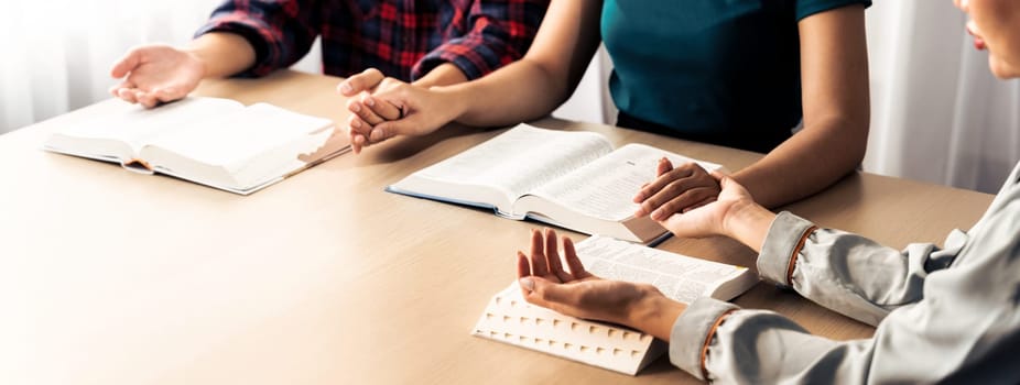 Cropped image of diversity people hand praying together at wooden church on bible book. Group of believer hold hand together faithfully. Concept of hope, religion, faith, god blessing. Burgeoning.