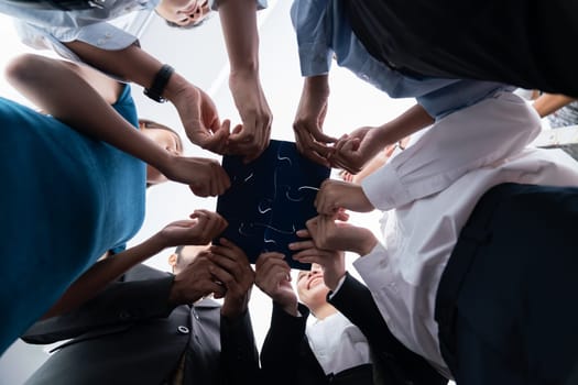 Below view of diverse corporate officer workers collaborate in office connecting puzzle pieces as partnership and teamwork concept. Unity and synergy in business idea by merging jigsaw puzzle. Concord