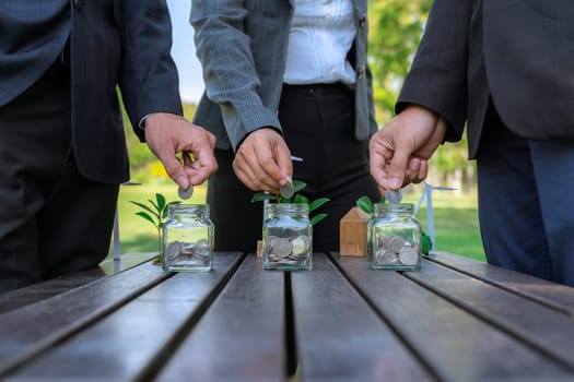 Business people put coin to money saving glass jar on outdoor table as sustainable money growth investment or eco-subsidize. Green corporate promot and invest in environmental awareness. Gyre