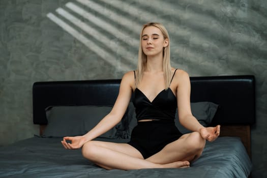 Young woman doing morning yoga and meditation in her bedroom, enjoying the solitude and practicing meditative poses. Mindfulness activity and healthy mind lifestyle. Blithe