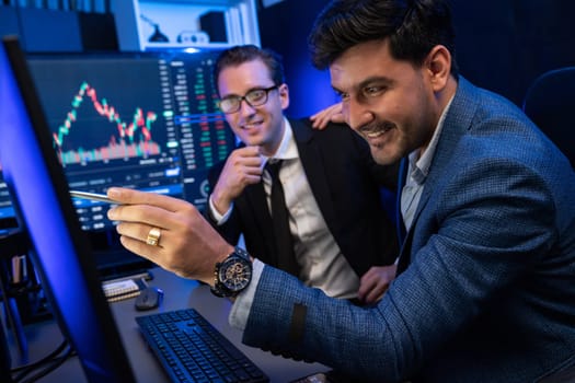 Two stock exchange traders discussing on dynamic successful investment graph, pointing trending of high profit in currency stock in financial data on monitor in neon light at workplace. Sellable.