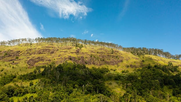 Aerial view of Mountain slopes with tropical forest and tea plantations under blue sky and clouds. Sri Lanka.