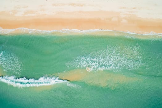 Aerial top down view of turquoise ocean wave reaching the coastline.