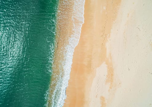 Aerial top down view of turquoise ocean wave reaching the coastline.