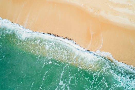 Aerial top down view of turquoise ocean wave reaching the coastline.