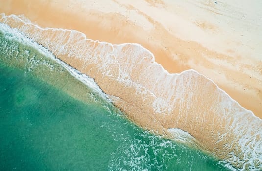 Aerial top down view of turquoise ocean wave reaching the coastline.